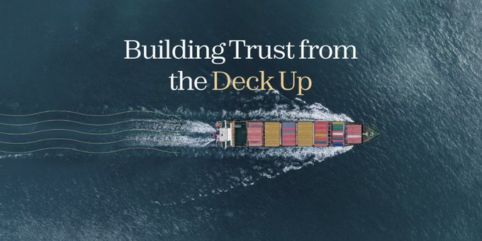 An aerial view of a cargo ship loaded with colorful containers sailing across the ocean, with the text 'Building Trust from the Deck Up' overlaid.