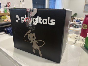 A black Playgitals box with the iconic Mewtwo silhouette sits on a desk, revealing the surprise gift referenced in the post—a tokenized collectible package from the Playgitals platform. The box features the "Playgitals" branding and the recognizable Pokémon character artwork, matching the "goodies" the user mentioned receiving unexpectedly.