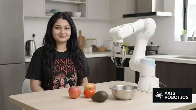 A woman in a Cannibal Corpse shirt sits at a kitchen table with apples, an avocado, and a metal bowl, alongside a white robotic arm; the Axis Robotics logo appears in the bottom right.