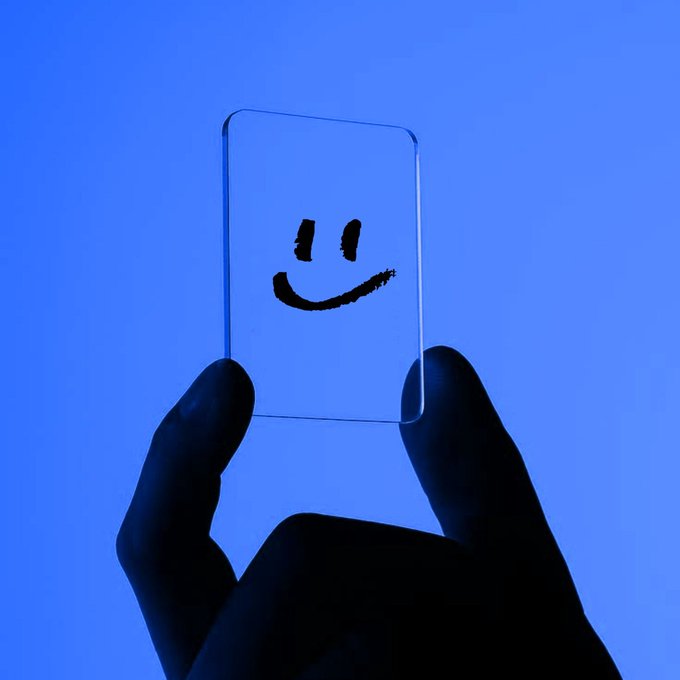 A hand holds up a clear card featuring a simple black smiley face against a bright blue background, symbolizing the friendly, user-focused experience of the newly launched browser extension that unifies searchable context across AI platforms and the web.