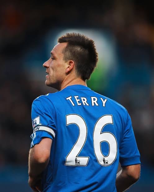 Football player John Terry wearing a blue Chelsea jersey with 'TERRY 26' on the back, photographed from behind on the pitch.