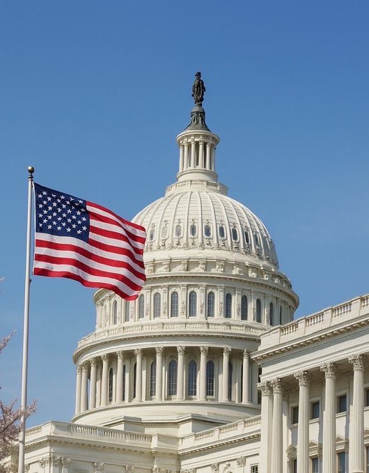 The U.S. Capitol dome stands beneath a clear blue sky, with the American flag waving in the foreground—symbolizing the legislative process where the comprehensive 616-page CLARITY Act is advancing toward a potential floor vote. The iconic setting underscores the bill's significance in merging Banking and Agriculture Committee versions to establish clearer regulatory guidelines.