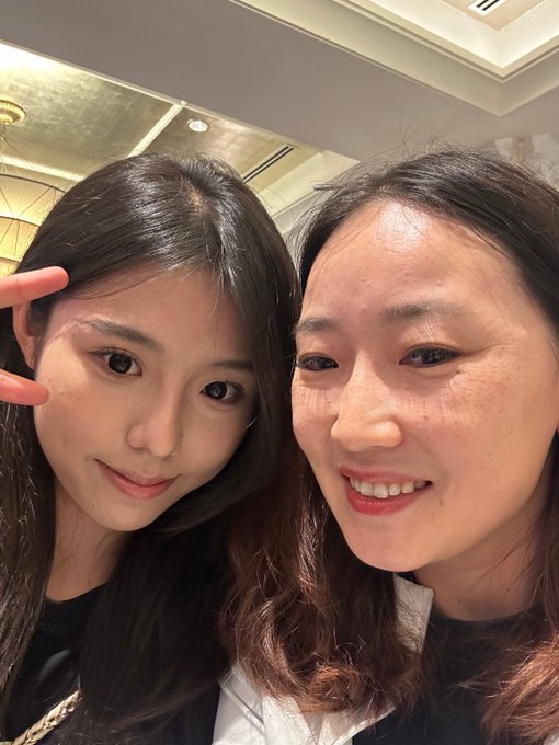 A selfie of two smiling young women, with one making a peace sign, taken indoors under warm lighting.
