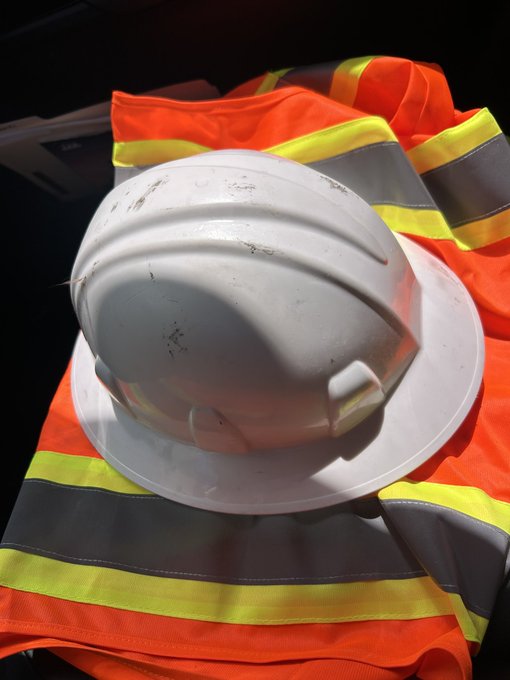 A white hard hat and a high-visibility orange safety vest sit together, with the post referencing $Sue, a BNB-chain memecoin, by playfully framing the construction PPE as the "memecoin mascot."