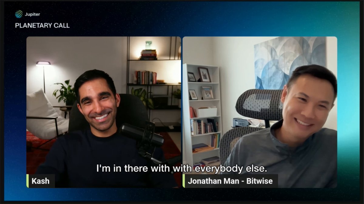 The image shows a man sitting down at a desk while talking to another person through a video call. The two men are smiling as they engage in conversation. The background of the image reveals that they are in a room with bookshelves, indicating an environment conducive for learning or working.