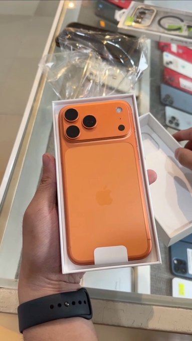 A hand holds an open box displaying a new orange iPhone, seemingly from an unboxing moment in an electronics store, paired with a thank-you post directed at Robinhood and NFTS.