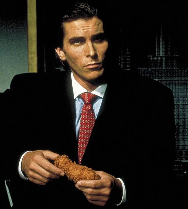 A man in a suit and red tie holds a corn dog, resembling Patrick Bateman from American Psycho.