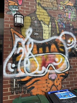 A tiger mural on a brick wall features bold graffiti-style lettering reading "CATS" and a signature tag "NEW ERA" along with "MURALS BY KRUST" at the top, tying into the post's description of the artist's role in pioneering "decentralized muralism" and bringing NFTs to the streets, with the small printer/scanner at the bottom likely used for sharing the NFT experience with passersby.