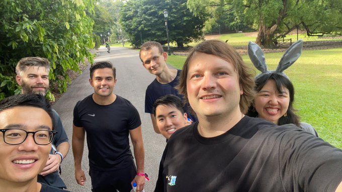 A group selfie taken in a park showing several people smiling, with one woman wearing bunny ears, on what appears to be a casual outdoor gathering.