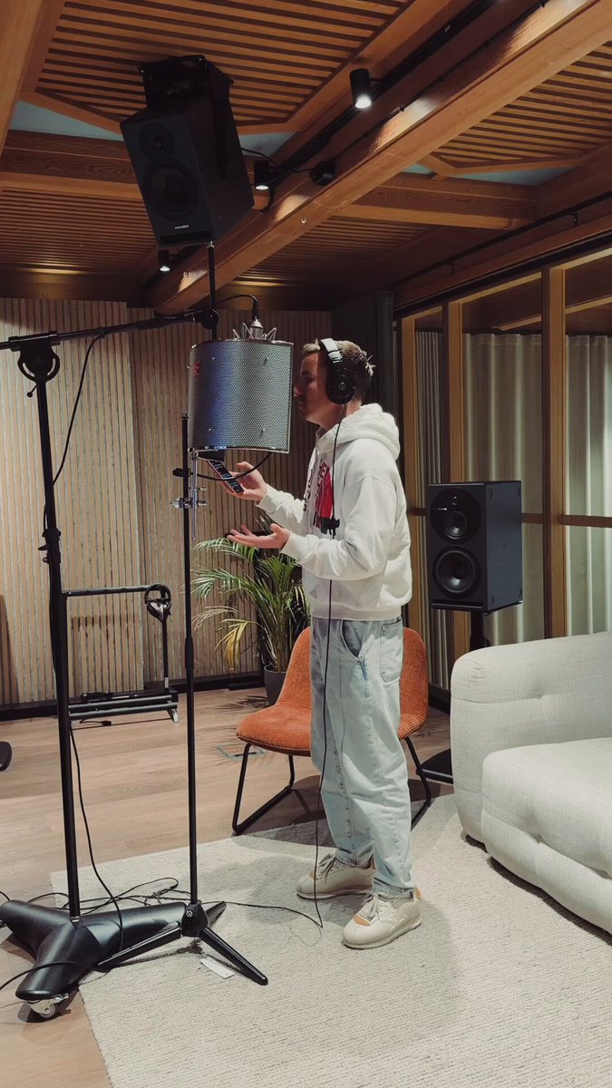 In the image, there's a person wearing headphones and standing next to an electronic music studio setup including a microphone stand and various speakers. This suggests that they might be preparing for or recording music. The surrounding area includes a couch placed against one wall with a potted plant nearby, indicating a cozy and comfortable environment. Although the post focuses on early Bitcoin prices and altcoins during the years 2015-2020, it does not directly relate to the scene in front of us regarding audio equipment and recording setups.