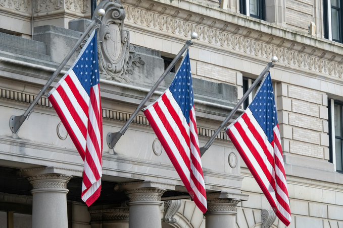 Three American flags hang from a classical stone building, symbolizing U.S. government involvement as the U.S. and UK unveil a 10-point roadmap to harmonize regulations on tokenized securities, stablecoins, and cross-border digital asset markets.
