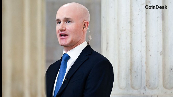 A bald man in a dark suit and blue tie speaks while wearing a small earpiece, standing before classical stone columns, with the CoinDesk logo visible in the upper right corner. The image accompanies a CoinDesk article about last-ditch efforts to push the Clarity Act, suggesting he is a key figure—such as a lawmaker or regulator—commenting on or involved in the legislative push for crypto market structure clarity.