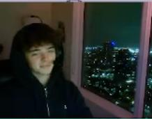 A blurry screenshot showing a young man with dark hair partially visible behind what appears to be glass or a window frame, with a dark cityscape visible in the background, allegedly shared as evidence by someone claiming they were "rugged" (scammed) by the pictured person during a livestream.