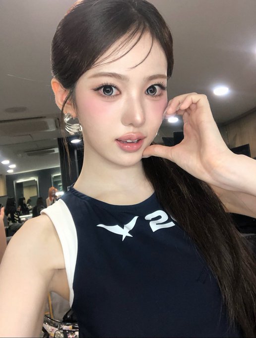 A close-up selfie of a young woman with long dark hair posing with her hand near her face, wearing a navy blue top featuring a white bird graphic and the number '2'.