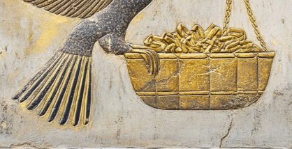 A detailed stone carving or relief depicts a bird with dark plumage carrying a golden woven basket filled with what appears to be gold coins or treasures.