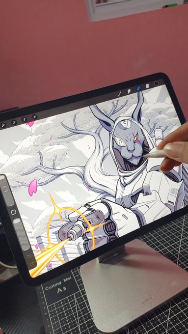 A hand uses a digital tablet to illustrate a white, futuristic deer character in a hooded jacket against a mountain landscape, with pink petals being added to the drawing.