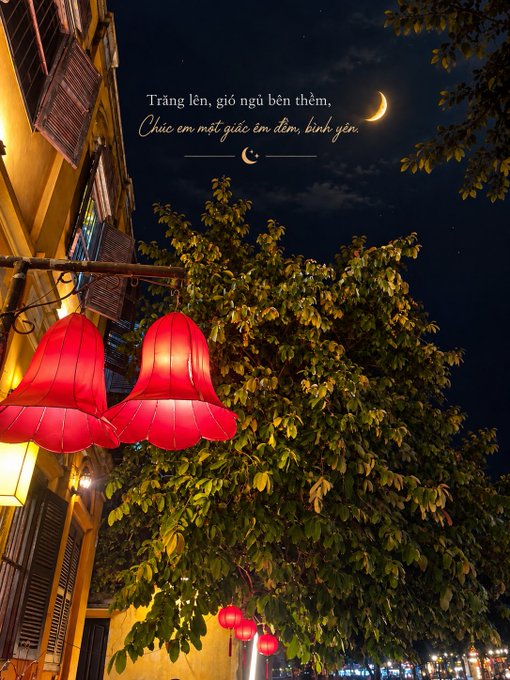 Red lanterns hang from a building near a tree at night, with Vietnamese text reading "Trăng lên, gió ngủ bên thềm, Chúc em một giấc êm đềm, bình yên" next to a crescent moon.