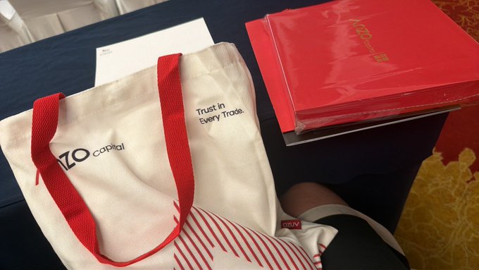A white tote bag with red handles displays 'IZO capital' and 'Trust in Every Trade.' alongside red folders on a blue table.