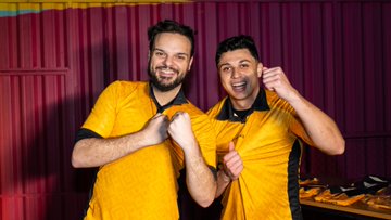 The image features two men wearing yellow shirts with black stripes standing close together against a red background, both smiling and holding hands. The text "Two passions. One community. Across the globe, the Binance community brought packed watch parties and pure love for the game to the opening matches." is present in the image. This suggests that the two men are passionate about soccer or sports in general, as they have gathered together to support their favorite teams at a sporting event. The post also mentions "Binance" and "Score With Binance," which could be related to the sport of soccer or possibly another popular online marketplace.