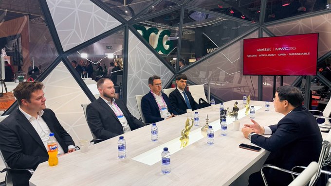 A business meeting takes place at MWC (Mobile World Congress), with a screen displaying "Viettel MWC 25 - SECURE. INTELLIGENT. OPEN. SUSTAINABLE" visible in the background, as five professionals in business attire sit around a conference table discussing telecommunications matters. The image visually represents the Viettel-Telcoin partnership discussions mentioned in the post, showing the type of executive-level meetings held at the conference.
