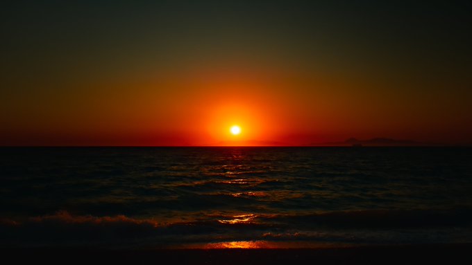 A scenic photograph of a vibrant orange sunset over the ocean, with the sun's reflection creating a path of light across the dark water.