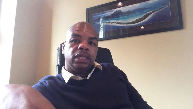 A man, identified as Davinci Jeremie, sits in a chair speaking to the camera, with a landscape painting of mountains and water hanging on the wall behind him. The image appears to be a still from a video discussing his early 2013 Bitcoin prediction and his YouTube channel content.