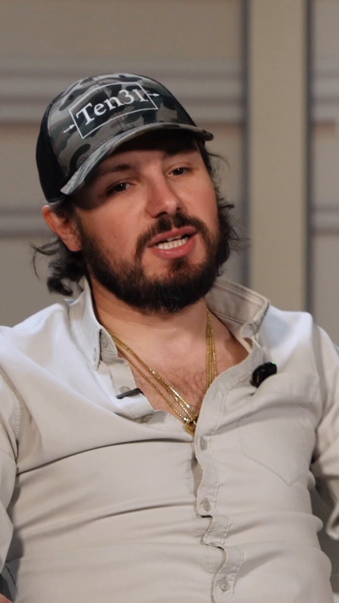 The image features a man wearing a white shirt with a black baseball cap and a gold chain necklace. He has a beard and appears to be smiling, possibly posing for a photo or participating in an interview. The caption of the image reads "If two billion people are using Ark and they're making Lightning payments, is that Lightning scaling? I think that's lightning scaling," which suggests that the man might be discussing the impact of Ark on the cryptocurrency market or the potential growth of the cryptocurrency industry.