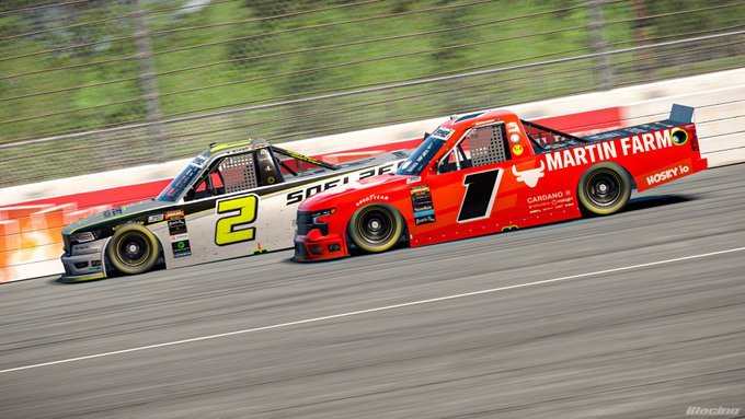 The image shows two race cars, one red and one gray, racing down a track during an event. The red car has the number 2 on its side, while the gray car has the number 1. Both cars are moving at high speeds, creating a sense of motion in the scene.