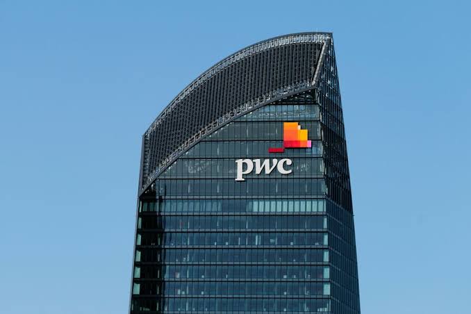 A tall glass skyscraper displaying the 'pwc' (PricewaterhouseCoopers) logo against a clear blue sky.