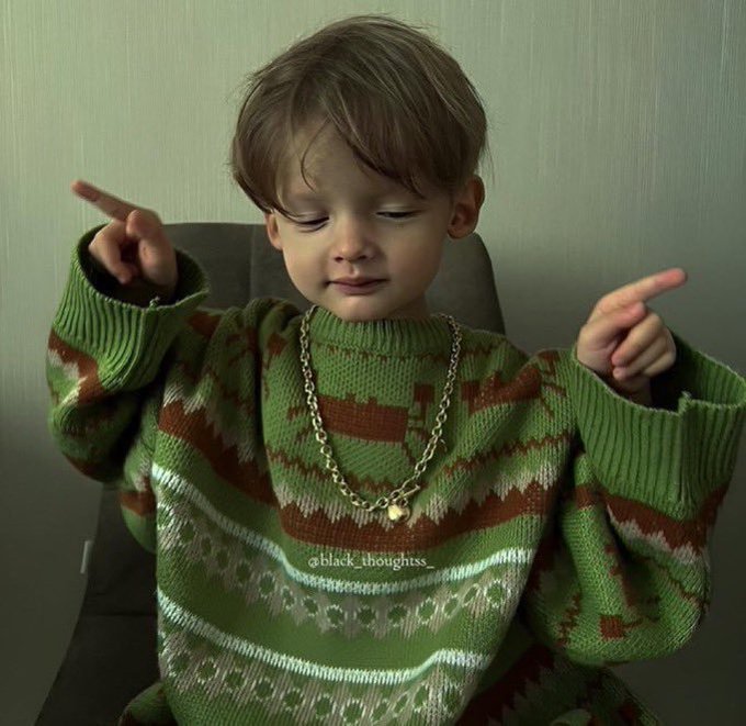 A young boy in a green patterned sweater and gold chain making a gesture, with the watermark '@black_thoughtss'.