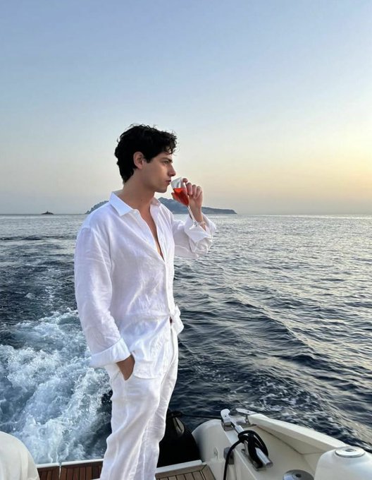 A man in a white linen outfit sips from a glass while standing on a boat at sea during sunset. The relaxed, luxurious scene aligns with the "happy saturday" vibe of the post, pairing a carefree weekend moment with a "gm web3" greeting.