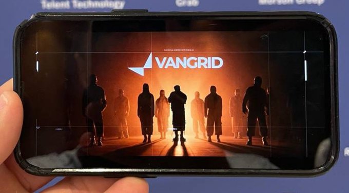 A hand holds a smartphone displaying the 'VANGRID' logo above silhouettes of people in a glowing room, with 'Talent Technology' and 'Grab' visible in the background.