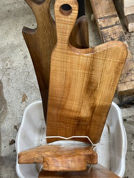 A handcrafted wooden cutting or serving board with a handle, standing upright and resting on a white plastic stool.