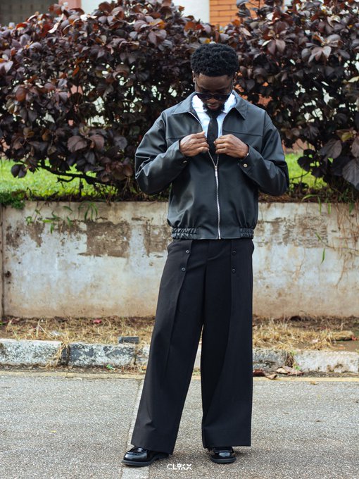 A stylish man in a dark blouson jacket, white collared shirt, black tie, and wide-leg trousers buttons up his jacket on a paved street, with the watermark "CLICK" visible at the bottom.

The caption "Project successfully attacked" playfully suggests the figure is gearing up or preparing for action, mirroring the determined, tactical look of his layered, uniform-inspired outfit.