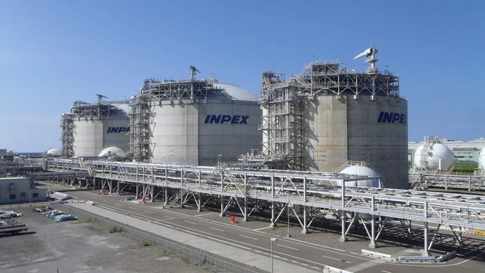 An industrial facility featuring large storage tanks branded with 'INPEX', with pipes and spherical tanks visible under a clear blue sky.