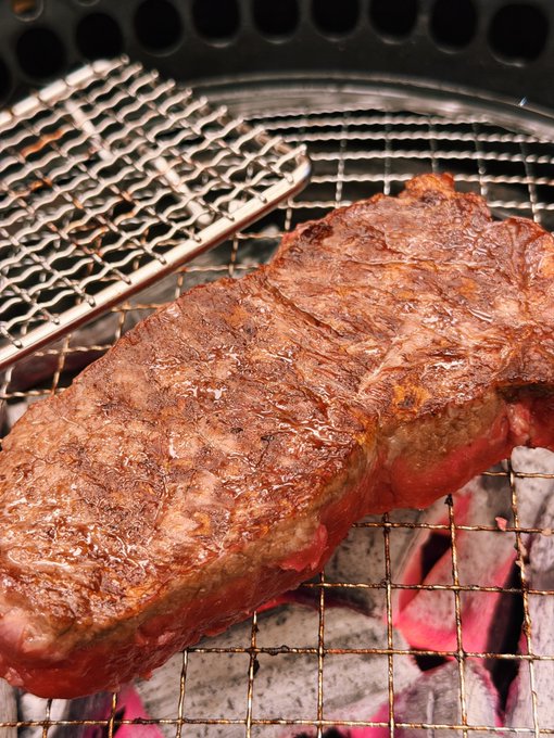 A close-up of a thick, well-seared steak cooking on a wire grill over glowing red-hot charcoal.