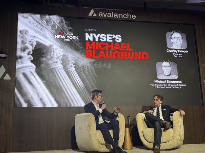 Two men sit on stage at the Avalanche Summit New York 2025 fireside chat, with a large screen behind them displaying "NYSE's Michael Blaugrund" and identifying Charley Cooper as President of Ava Labs and Michael Blaugrund as Vice President of Strategic Initiatives at the Intercontinental Exchange, visually capturing the discussion about NYSE's interest in an on-chain future.