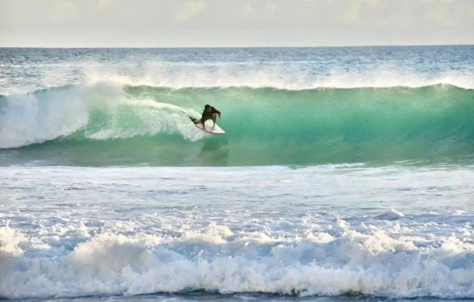 A lone surfer carves through a curling turquoise wave, dwarfed by the powerful ocean. The image contrasts the surfer's solitary thrill with the post's reflection on lost fortunes and personal change—both suggesting the passage of time and the fleeting nature of past pursuits.