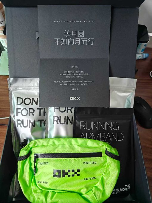 An OKX promotional gift box containing running-related items including a green fanny pack, running armband, and a 'Happy Mid-Autumn Festival' greeting card with Chinese text '等月圆 不如向月而行'.