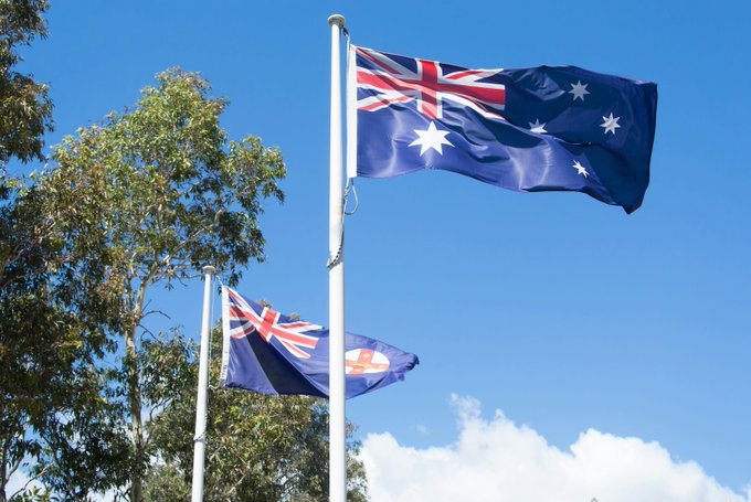 Two Australian flags fly against a bright blue sky with scattered clouds, symbolizing Australia's regulatory action against Cryptolink as AUSTRAC suspends the crypto ATM operator's registration for failing to meet reporting requirements.