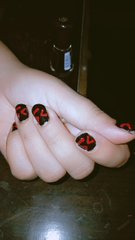 A close-up of a hand displaying black nail art with red bow designs on dark fingernails.