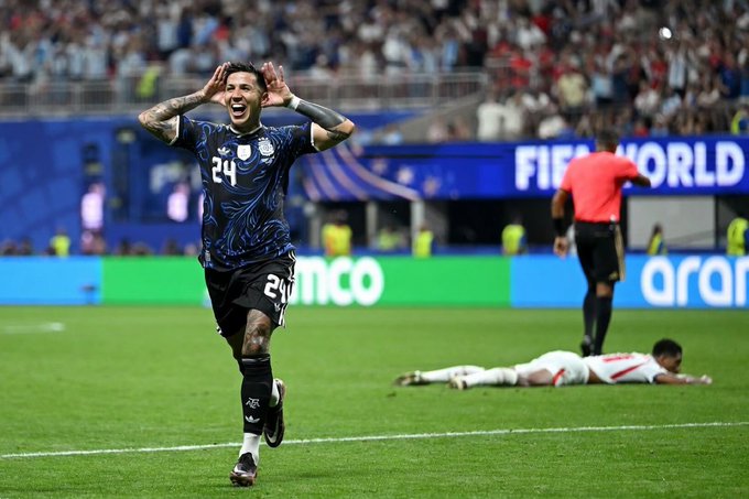 Soccer player wearing Argentina's #24 jersey celebrates with hands to his face in triumph, with a 'FIFA WORLD' banner and 'aramco' advertisement visible on the pitch.