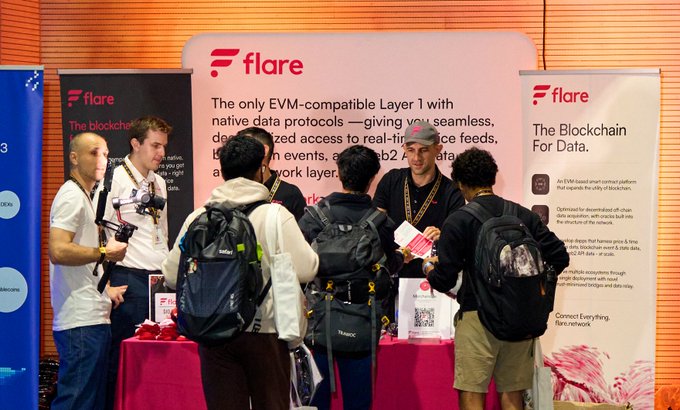 A bustling exhibition booth for 'Flare, The Blockchain For Data,' featuring an EVM-compatible Layer 1 platform, where a representative interacts with attendees who are holding brochures.