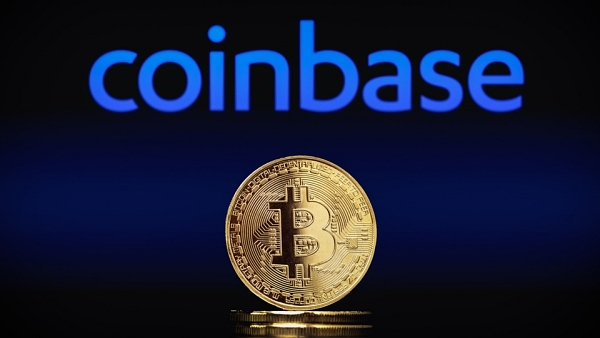 A stylized image showing a physical Bitcoin coin in the foreground with the Coinbase logo prominently displayed in blue against a dark background.