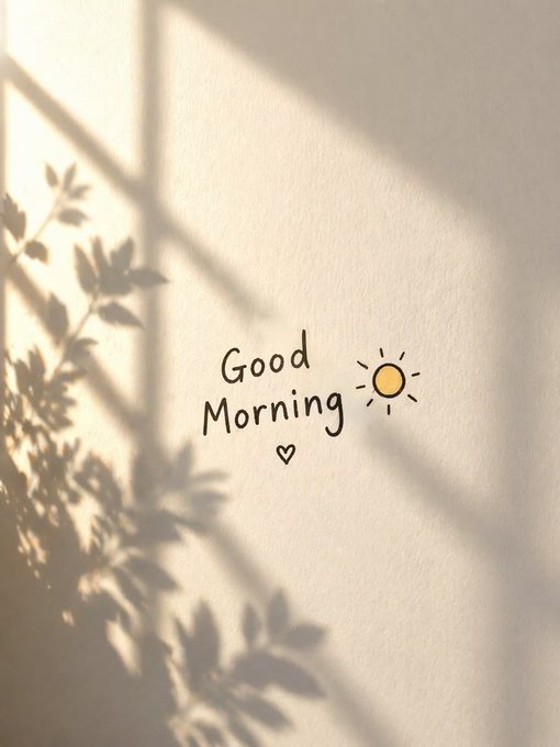 A minimalist 'Good Morning' illustration with a small sun and heart, cast with soft window and leaf shadows on a cream wall.