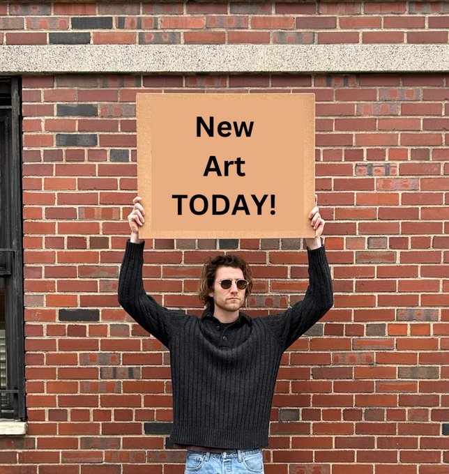 A young man with sunglasses and a black sweater holds up a brown cardboard sign reading 'New Art TODAY!' against a red brick wall.