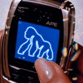A finger taps a phone screen displaying a glowing blue outline of an ape, with the text "APE" at the top—visually echoing the post's call to action to "Pick up $APE" and highlighting the ape-themed branding of the ApeChain ecosystem.