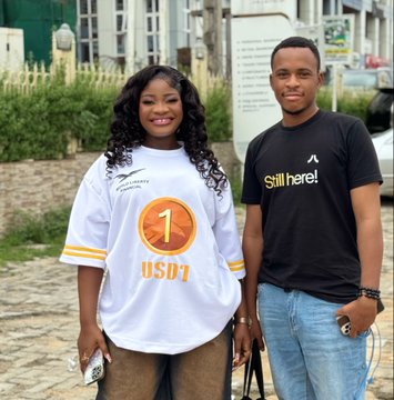 The image shows a woman in a "USD1" jersey and a man wearing a "Still here" t-shirt posing together in Abuja, illustrating the post's narrative of an on-the-street World Liberty Financial / USD1 promotion, with the woman highlighting her interview (likely conducted by the other person, @bennie_4evar) and showcasing the sponsored "Still here" tee.