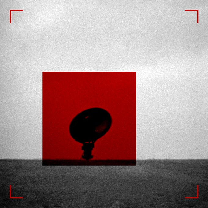 An artistic image showing a red square containing a dark silhouette, framed by red brackets against a grayish background, resembling a camera viewfinder.