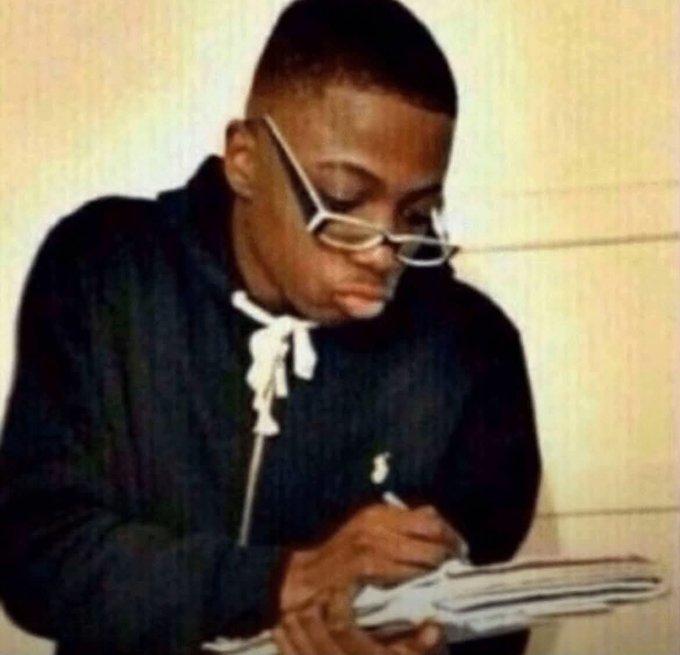 A young man wearing a black hoodie, distinctive white-rimmed glasses, and a cross necklace is shown writing in a notebook in what appears to be a vintage photograph.